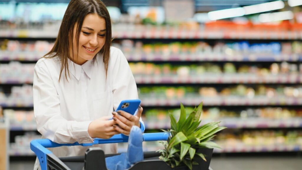Woman shopping with grocery cart and phone