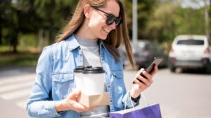 Woman carrying coffee and smiling at her phone