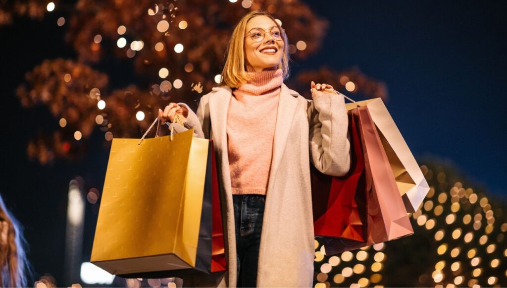 Woman in front of holiday lights with shopping bags