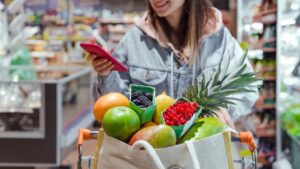 Woman looking at phone while grocery shopping with cart full of food