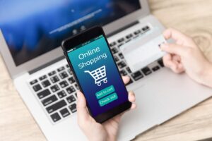 Woman holding credit card and mobile phone above laptop while online shopping, showing digital customer journey.