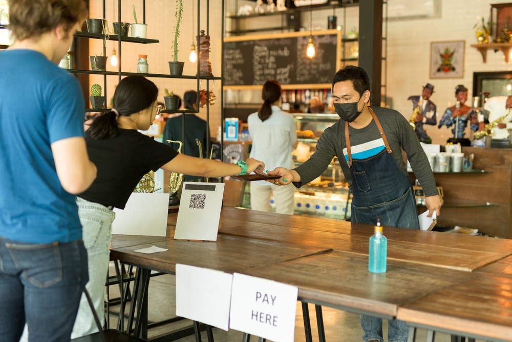 A coffeeshop adapting to the changes in consumer behavior post-COVID-19, as shown by customers wearing masks and paying for items contactless and from a distance.